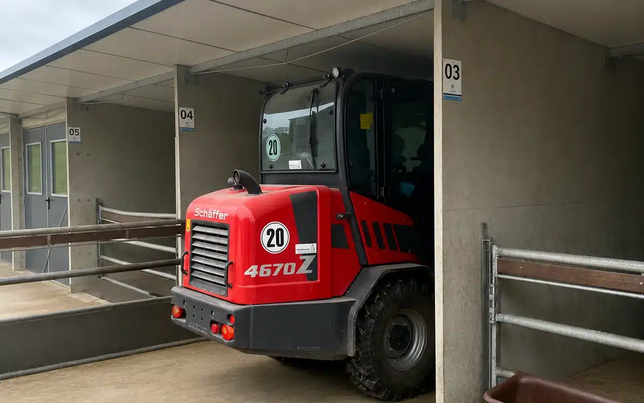 Een shovel rijdt een afdeling van de Optima Klima Stal in om uit te mesten